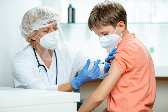 Female doctor in full protective workwear injecting vaccine into boy's arm